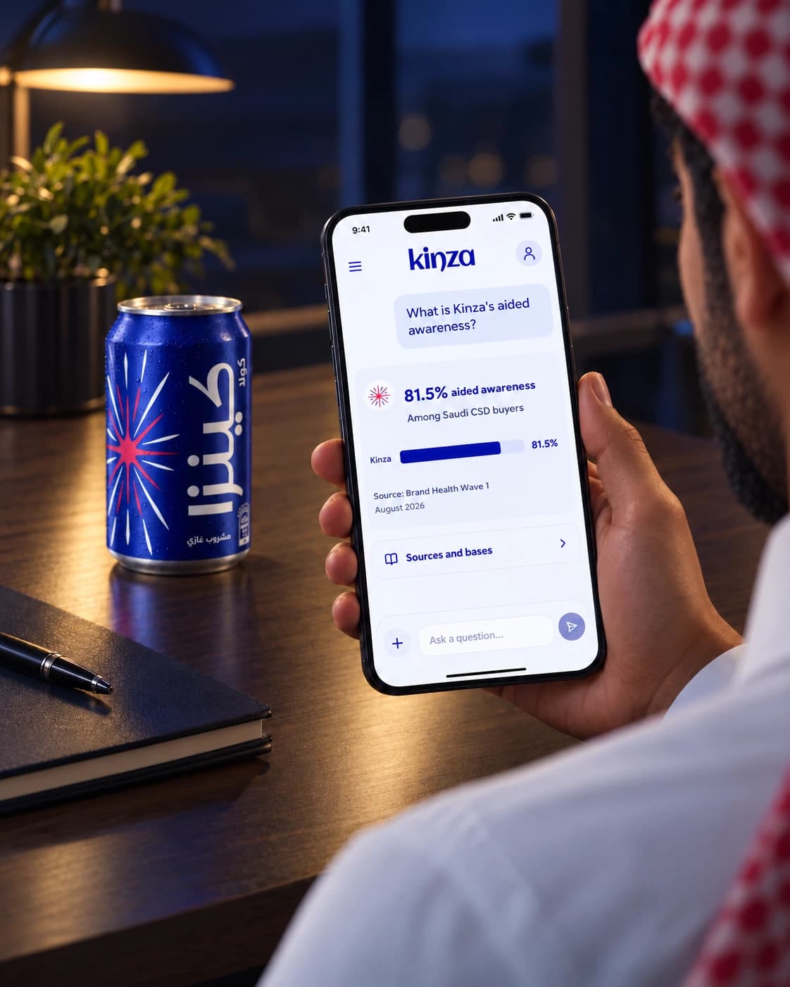 A hand holding Kinza research insights on a phone beside a Kinza cola can
